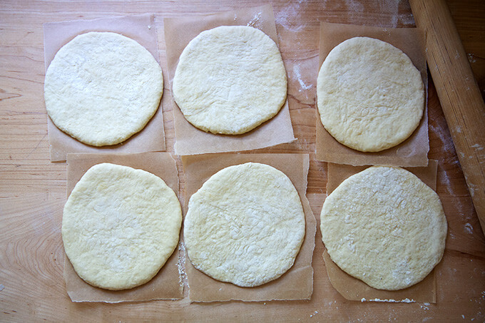 Six rounds of unbaked pita, each on a sheet of parchment paper.