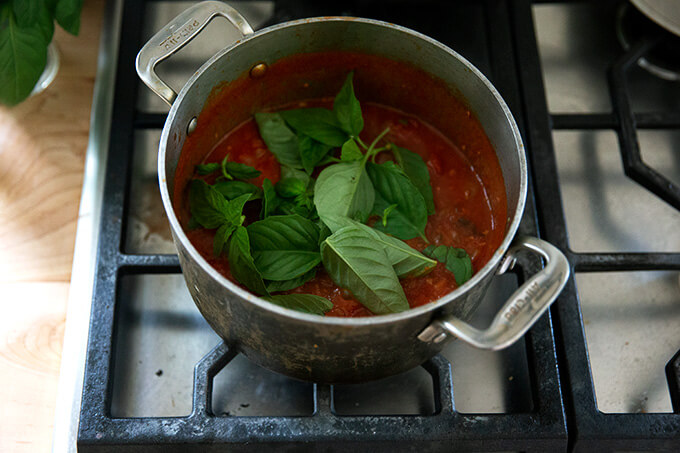A pot of tomato sauce simmering stove top with fresh basil added.