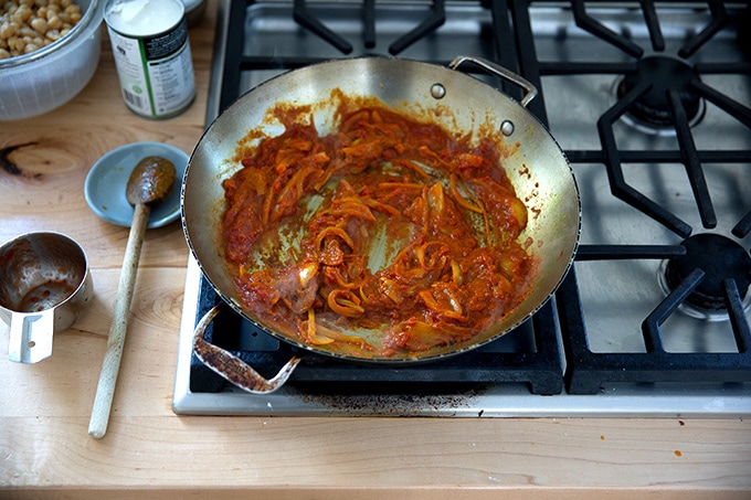 A skillet on the stovetop with onions, spices, and Thai red curry paste.