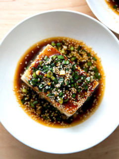 A bowl of warm tofu topped with sesame scallion sauce.