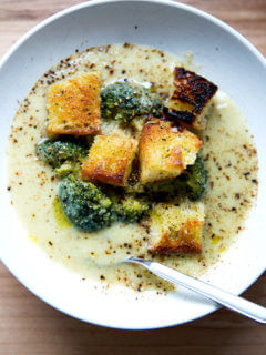 A bowl of broccoli-cheddar soup with olive oil toasted croutons and a spoon.