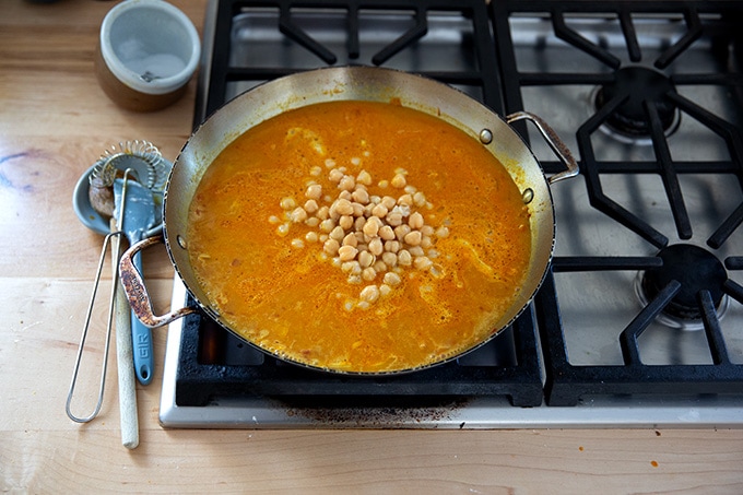 A skillet on the stovetop holding the makings of curried Thai chickpeas.