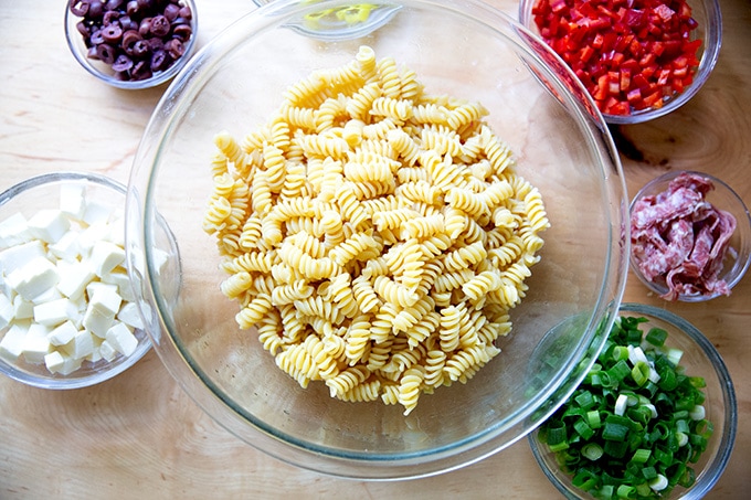 The components of a deli-style pasta salad, each in separate bowls on a countertop.