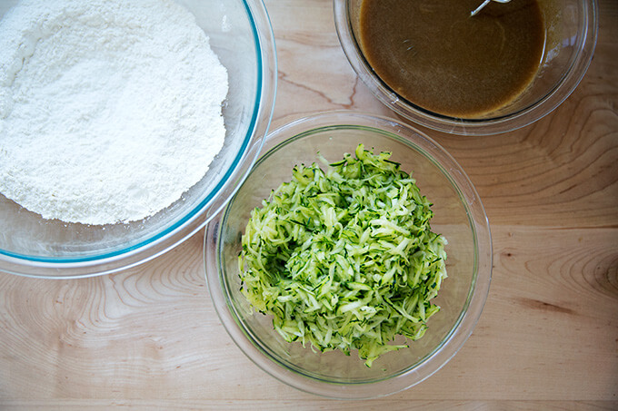 Components to make zucchini bread: dry ingredients, wet ingredients, grated zucchini.
