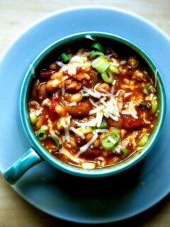 A bowl of spicy, smoky stovetop vegetarian chili with cheese and scallions stirred in.
