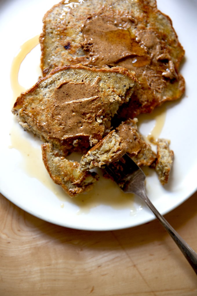 Banana-oat pancakes on a plate with almond butter and maple syrup.