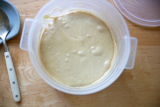 A two-quart container holding just-stirred sourdough starter aside a large spoon.
