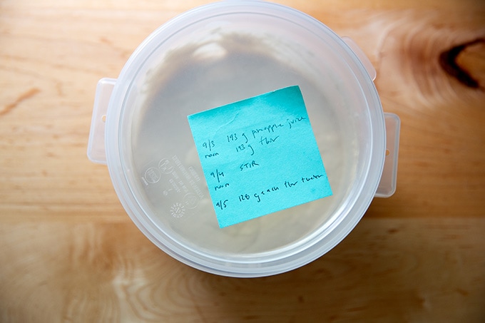 A two-quart container holding sourdough starter, covered with a post-it note on top.