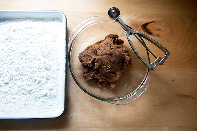The "batter" for the rum balls in a bowl aside a powdered-sugared filled tray.