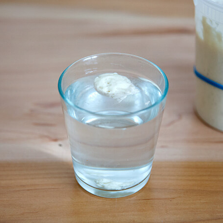 A cup of water holding a spoonful of sourdough starter floating. 