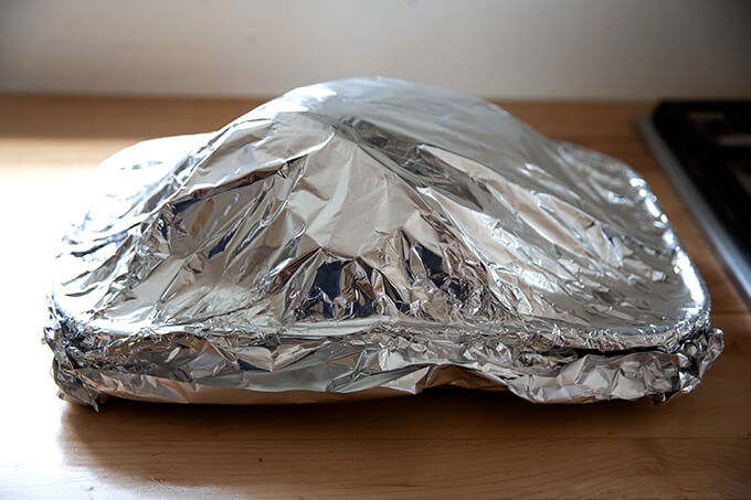 A roasting pan holding a ham, covered in foil.