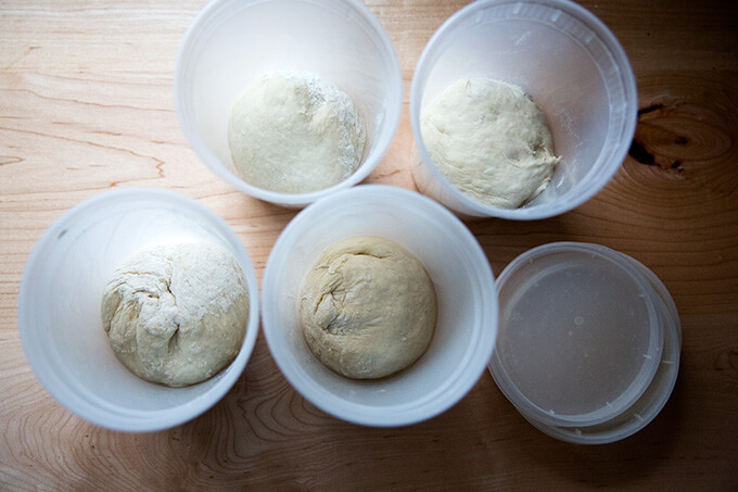 Four quart containers holding rounds of homemade pizza dough.