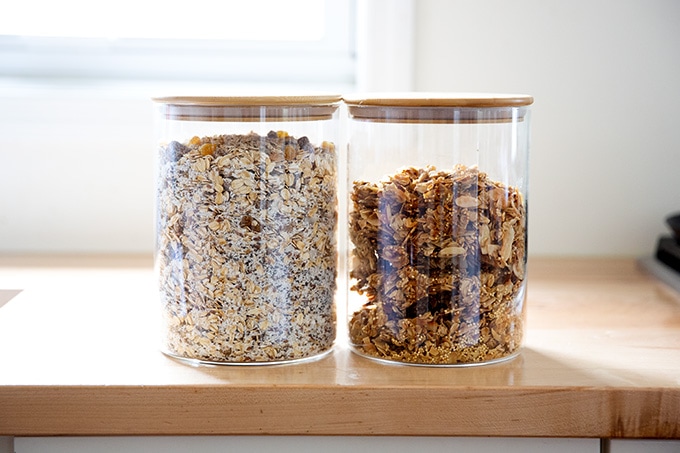 Two containers filled with muesli and granola on a countertop.