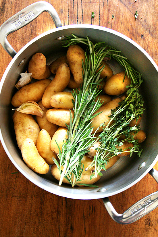 A pot filled with potatoes, herbs, and garlic. 