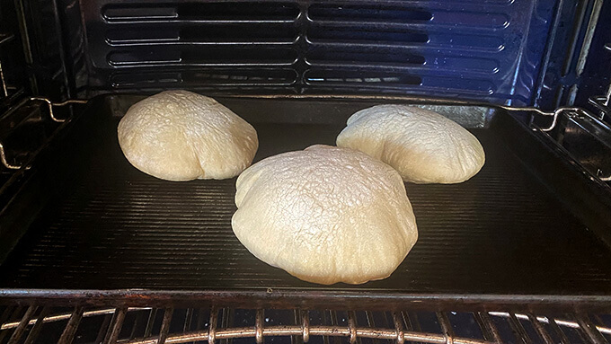 Three pita cooking on a preheated sheet pan in the oven. 