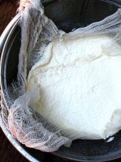 A cheese cloth-lined sieve holding homemade ricotta.