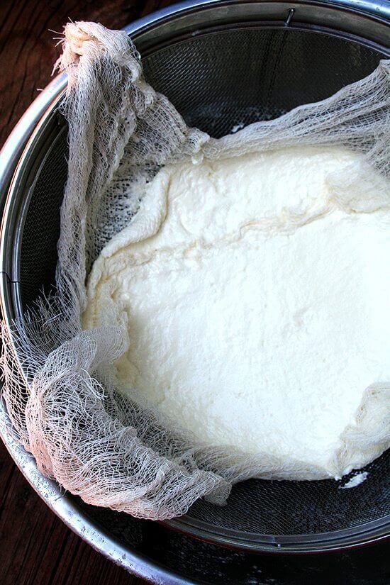A sieve lined with cheesecloth holding homemade ricotta.