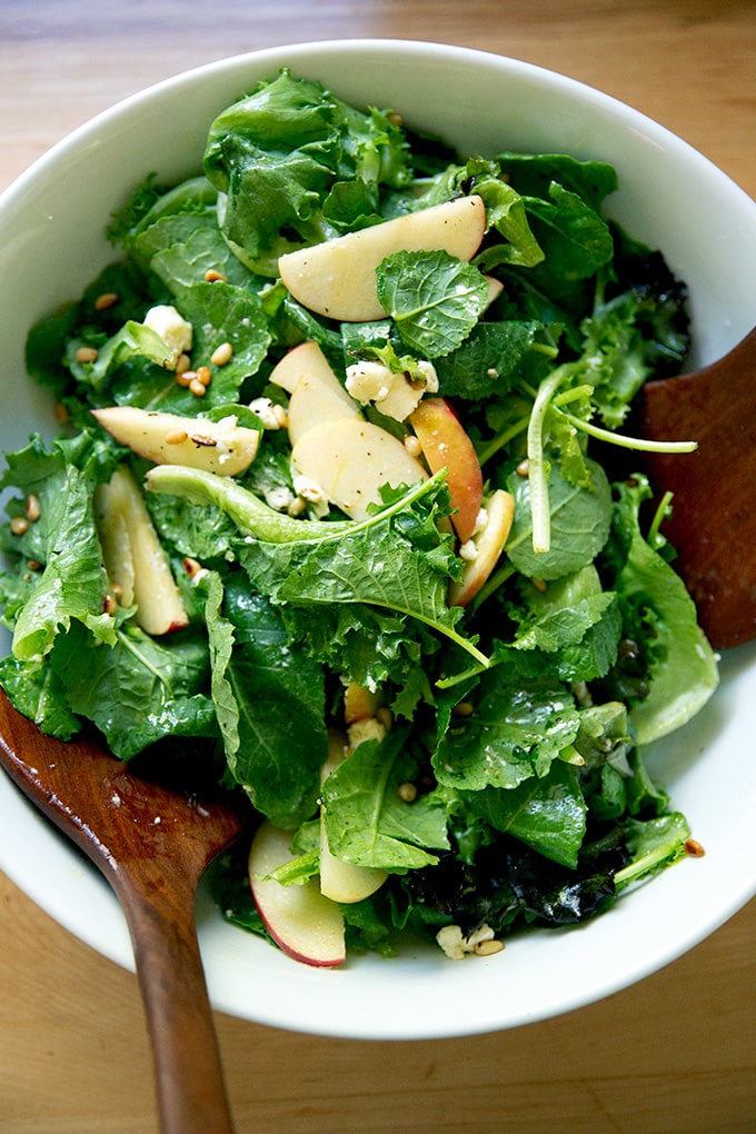 A fall salad of greens, pine nuts, goat cheese, and apples in a bowl.