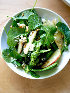 A fall salad of greens, pine nuts, goat cheese, and apples in a bowl.