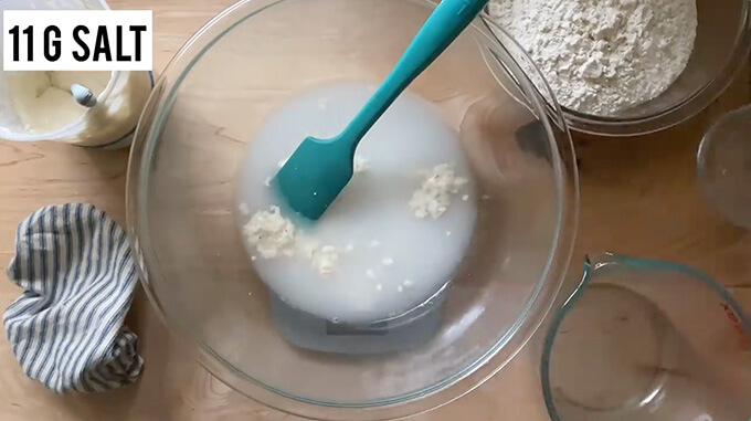 A bowl on a scale holding, water, salt, and sourdough starter all mixed together. 