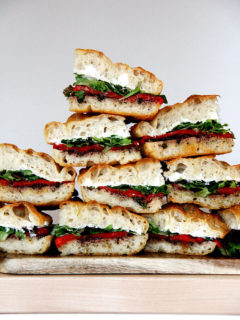 A stack of slab sandwiches with whipped honey goat cheese, roasted red peppers, olive tapenade and greens.