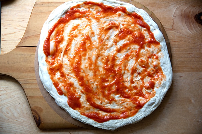 An unbaked pizza on a pizza peel lined with a parchment paper round.