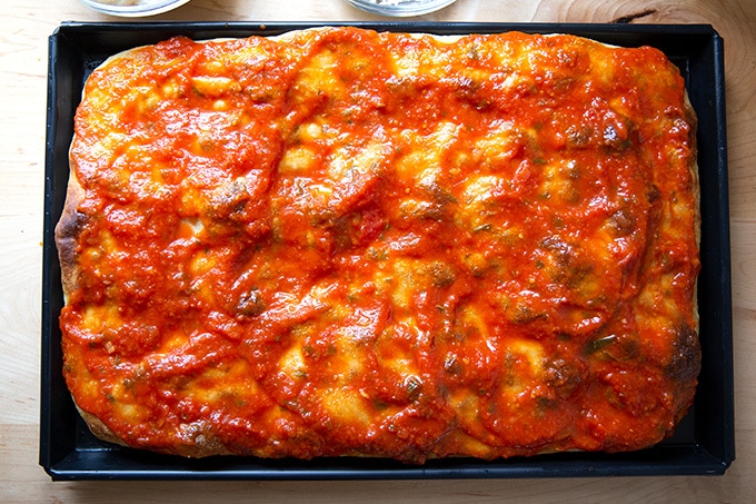 A sauced, parbaked slab of Sicilian-style pizza.