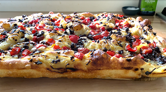 Baked pissaladière, side view, on a board.