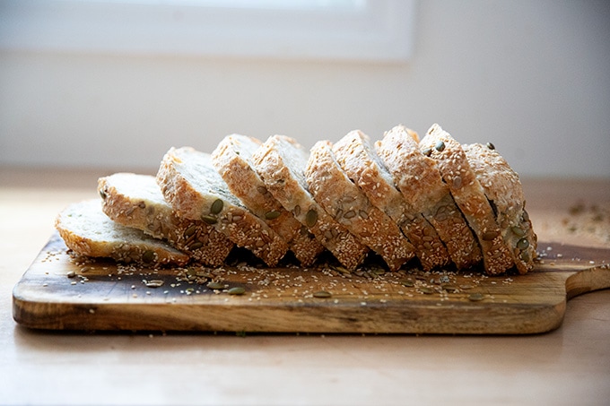 A sliced loaf of three-seed bread on a cutting board.