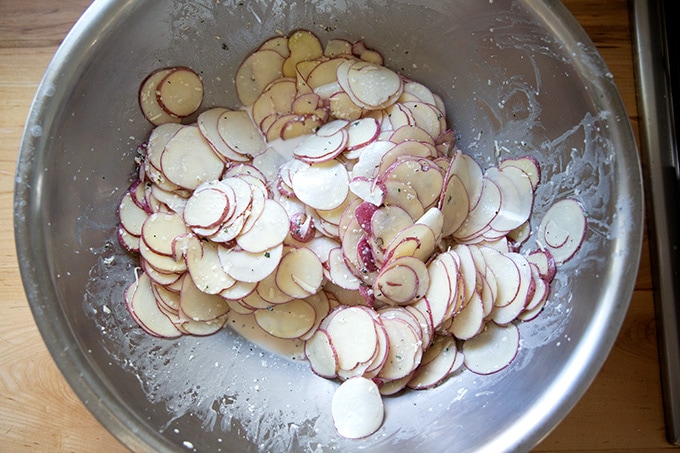 A very large bowl filled with sliced potatoes and ingredients to make potato gratin.