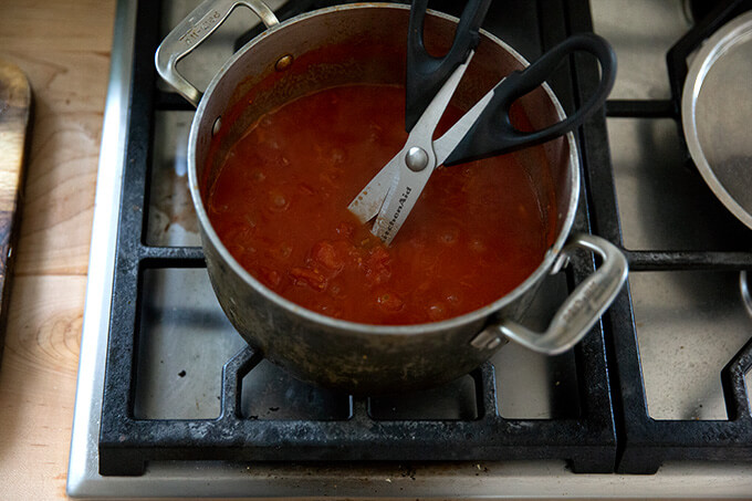 A pot of tomato sauce simmering stovetop with scissors inside.