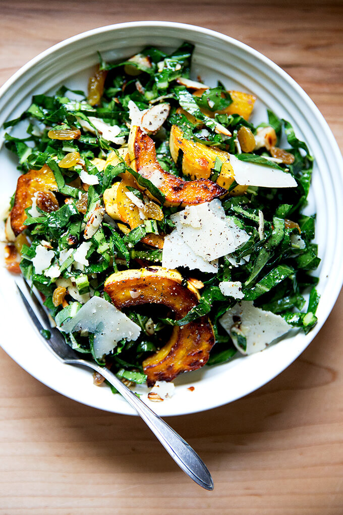 A bowl of raw collard green salad with roasted delicata squash, toasted almonds, golden raisins, and shaved parmesan.