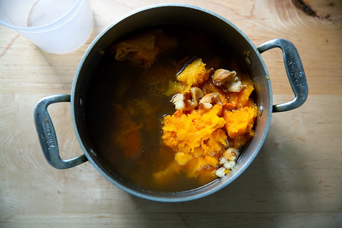 A soup pot filled with vegetable stock, roasted butternut squash, and roasted garlic.