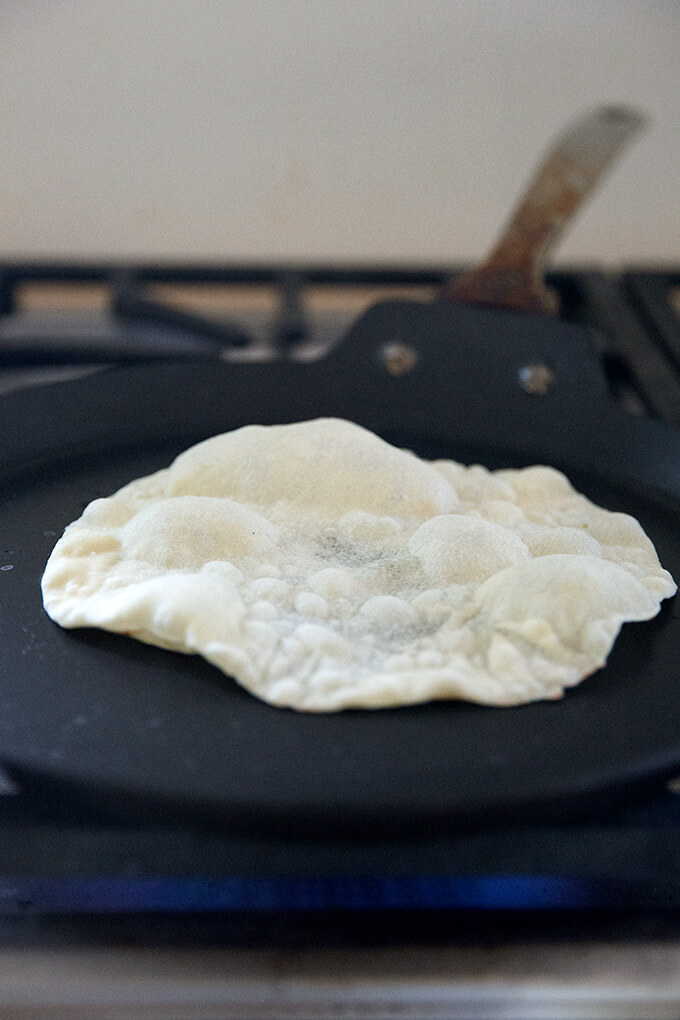 A sourdough tortilla cooking stovetop in a skillet.