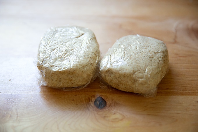 Two portions of sourdough cracker dough wrapped in parchment paper.